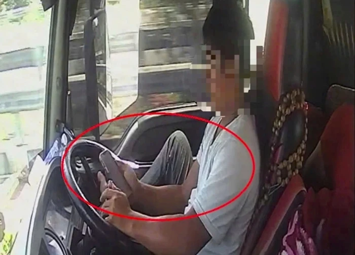 Tài xế dùng chân điều khiển xe đầu kéo chạy trên cao tốc, tay cầm điện thoại lướt TikTok